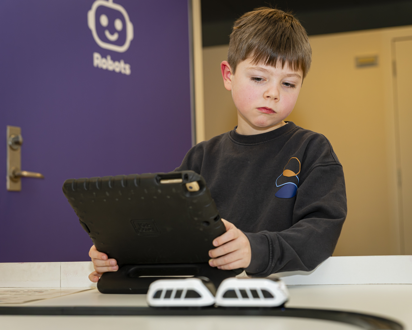 Een kind programmeert robots met een tablet bij de robotwand